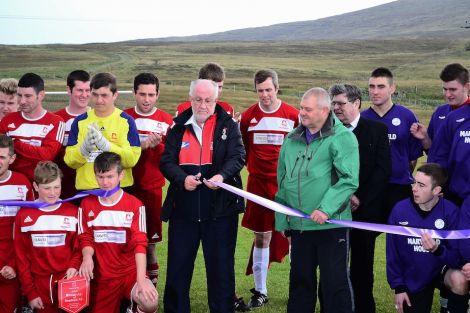 Bressay Sports Club chairman Kenny Groat looks proudly on as footballing veteran Jim Peterson cuts the ribbon to officially open the Bressay sports pitch. Photo Mark Berry