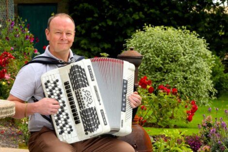 A man holding an accordion outdoors with a smile.