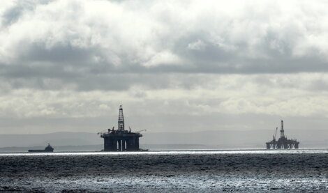 Offshore oil rigs and a supply vessel at sea under a cloudy sky.