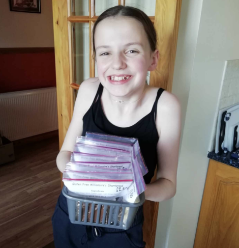 Young girl smiling and holding a stack of labeled packages in a kitchen.