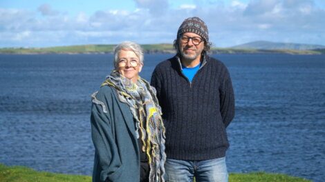 Two people standing by the water with a landscape view in the background.