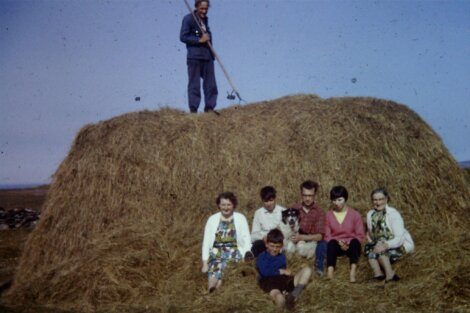 A family and their pets posing in front of a hay bale on a farm.