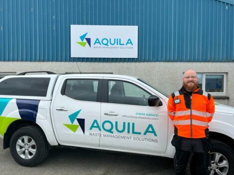 A man in a high-visibility vest standing next to a white pickup truck with the aquila waste management solutions logo.