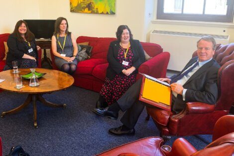Four professionals having a meeting in a sitting area with red sofas and drinks on the table.