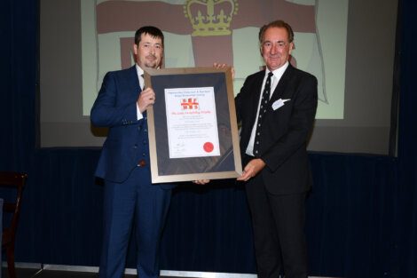 Two men in suits holding a certificate in front of a screen.