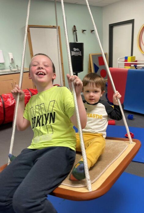 Two boys sitting on a swing in a playroom.