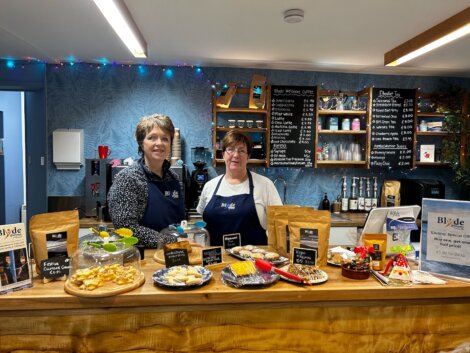 Two women standing in front of a counter with food.