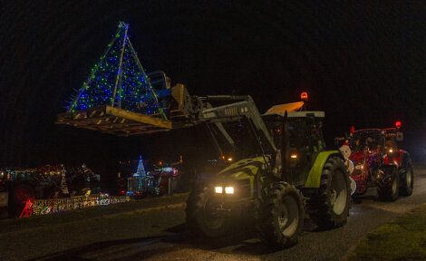 A tractor pulls a christmas tree down a road.