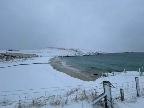 A beach covered in snow with a fence in the background.