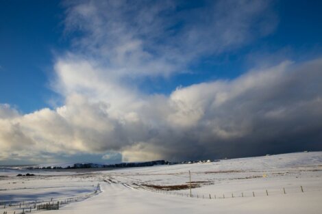 A snow covered field with clouds in the sky.