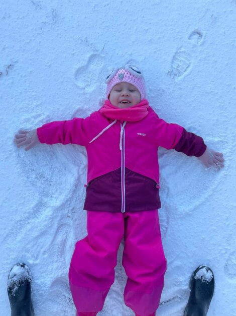 A little girl laying in the snow with her hands in the air.
