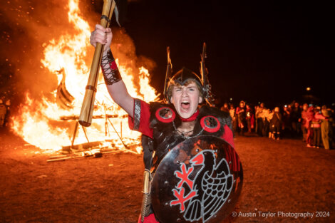 A man with a shield in front of a bonfire.