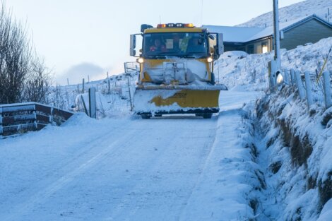 A snow plow driving down a snow covered road.