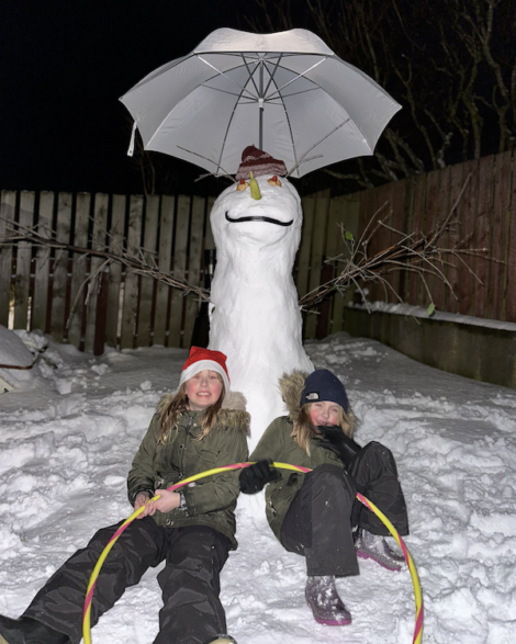 Two girls standing next to a snowman with a hula hoop.