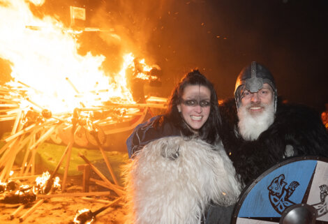 Two people standing in front of a fire.