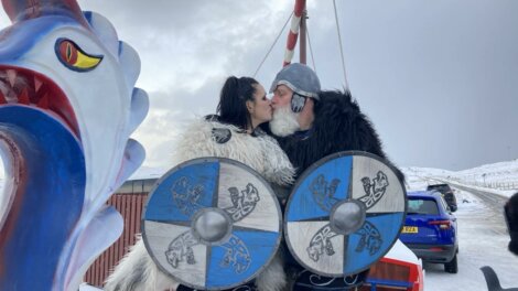 A couple kisses in front of a viking sleigh.