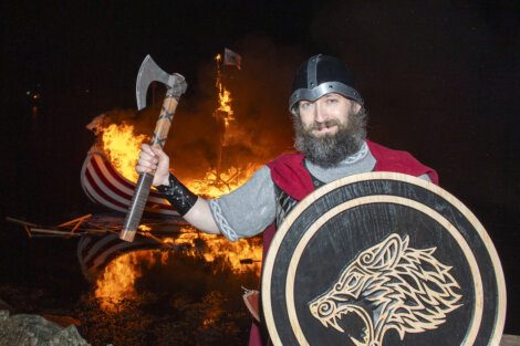 A man in a viking costume standing in front of a fire.