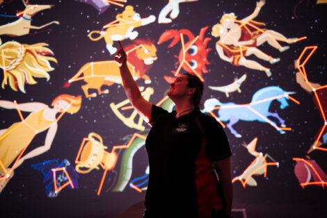 A woman is standing in front of a projection of constellations.