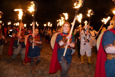 Participants dressed in costumes carrying torches during a nighttime procession.