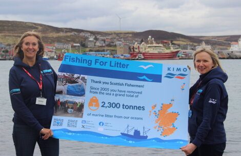 Two women standing outdoors, holding a sign that celebrates scottish fishermen for removing 2,300 tonnes of litter from the ocean.