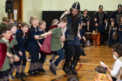 Children participate in a playful reenactment with a person dressed as a viking during a historical demonstration.